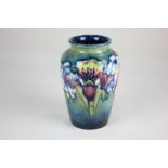 A Moorcroft pottery tapered vase decorated with orchids and smaller blue flowers, on green and