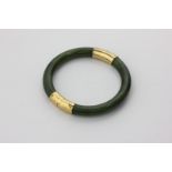 A jade bangle with yellow metal hinged mounts