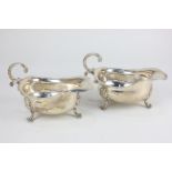 A pair of George V silver sauce boats with flying scroll handle, on three foliate cast paw feet,