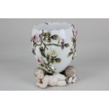 A 19th century porcelain vase on three nude cherub support with climbing rose bocage design, 14.