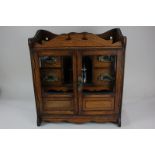 A 20th century oak smoker's cabinet, the bevelled glass doors enclosing four drawers and a pottery