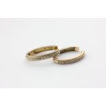 A pair of diamond oval hoop earrings set with a line of round diamonds on white and yellow gold