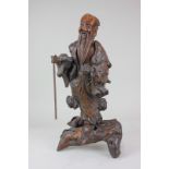 A Chinese carved gnarled wood figure of a sage holding a staff, atop a piece of wood, 55cm