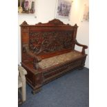 An impressive carved oak settle with high panelled back decorated with griffin, fruiting branches