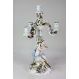 A Sitzendorf porcelain three-branch candelabra modelled as a winged cherub holding aloft a