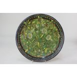 A Doulton Lambeth pottery charger by Mary Capes, decorated with daisies and other flowers within a