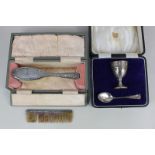 A cased George V silver egg cup and spoon, Birmingham 1922, a cased dressing table brush, and silver