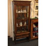 An oak display cabinet with scrolling foliate carved frieze and panel glazed door enclosing three