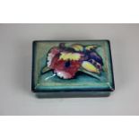 A Moorcroft pottery rectangular trinket dish and cover decorated with an orchid on blue and green