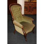 A Victorian button back fireside armchair with padded arms, on cabriole front legs and castors