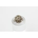 A diamond cluster ring, the round brilliant cut stone twelve-claw set within a baguette and