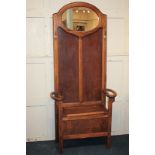 An oak effect hall stand, the raised panel back with oval mirror and two coat hooks above a bench