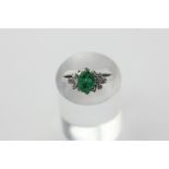 An emerald and diamond ring in 18ct white gold, the oval cut stone with clusters of brilliant cuts