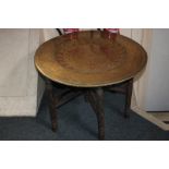 An Eastern circular side table with dished and floral engraved brass top, resting on folding base