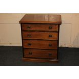 A small mahogany chest of four drawers with circular embossed back plates and brass ring handles, on
