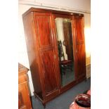 A mahogany triple door wardrobe, with central full length mirror door, flanked by panelled doors,