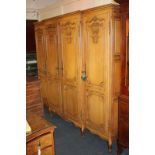 A light oak armoire style break-front wardrobe with four shell and scroll carved panelled doors