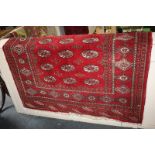 A Bokhara wool rug with three rows of elephant foot motifs within multiguard border, on crimson