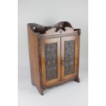 An oak smoker's cabinet with two carved panel doors enclosing two small drawers, shelf and rack,