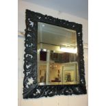 A carved ebonised wall mirror, rectangular shape with pierced shell and foliate border, bevelled