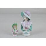 A porcelain half doll of a lady wearing a feathered hat and pink shawl, 12.5cm, and another similar,