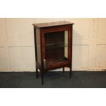 An Edwardian walnut small display cabinet with glazed panel door enclosing glass shelf, on square
