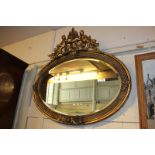 A gesso and giltwood oval wall mirror, with pierced foliate and figural surmount, mirror plate, 52cm