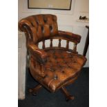 A button upholstered brown leather office chair, with raised back and padded arms on spindle