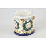 A small majolica glazed pot decorated in raised relief with putti and garlanded faces, initialled