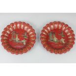 A pair of Chinoiserie red lacquered plates, each with moulded scalloped edge, decorated with figures