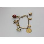 A 9ct gold bracelet hung with various charms including a South African one pound coin, 37.3g gross -