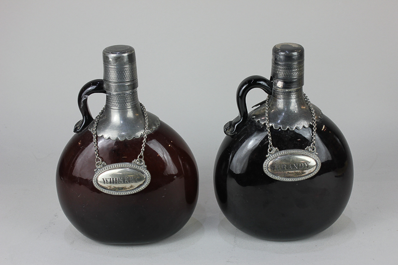 A metal mounted amber glass flask and another similar (with damaged spout), with labels for whisky