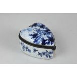 A 19th century Delft enamel heart-shaped patch box decorated in blue with a lady in a garden, on
