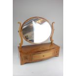 An oval mahogany inlaid toilet mirror on box base with bow front and three drawers, raised on