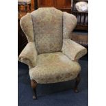 A wing back armchair with paisley type upholstery, on shell capped cabriole front legs to pad feet