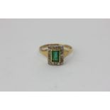 An emerald and diamond ring, the step cut stone rubover set in a border of eight-cut diamonds