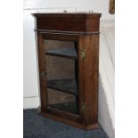 An oak hanging corner wall cupboard with glazed panel door enclosing two shelves, with 'H' shaped