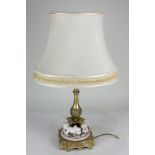 A gilt metal table lamp with leaf cast baluster stem resting on three porcelain recumbent putti,