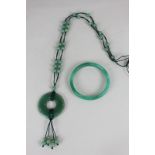 A jade bangle, and a jade pendant on a cord chain strung with groups of small jade beads