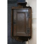 An oak hanging corner wall cupboard with small shelf surmount above panel door enclosing shelf, with