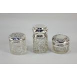 Three Edward VII and later silver lidded cut glass dressing table jars, one with embossed cherub