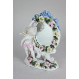 A Continental porcelain model of a cherub peering into an oval mirror, the frame and base