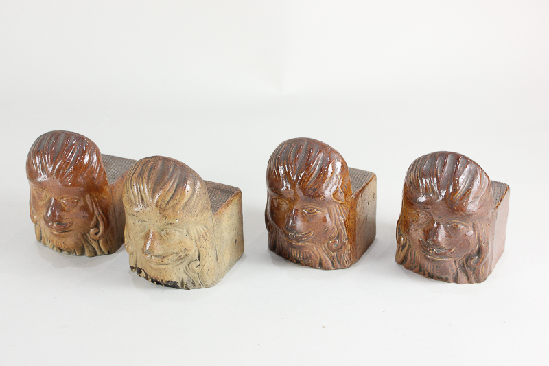 A set of four glazed pottery mask fronted furniture or pot stands, 5.7cm