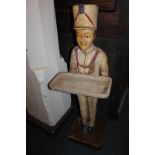 A carved and painted wooden dumb waiter in the form of a figure in uniform holding a tray, 104cm