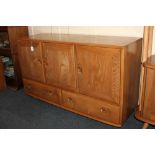 An Ercol elm sideboard, with three panel doors enclosing cupboards, and two drawers below, on