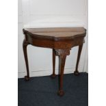 A reproduction crossbanded walnut card table, demi-lune shape with fold-over green baize lined