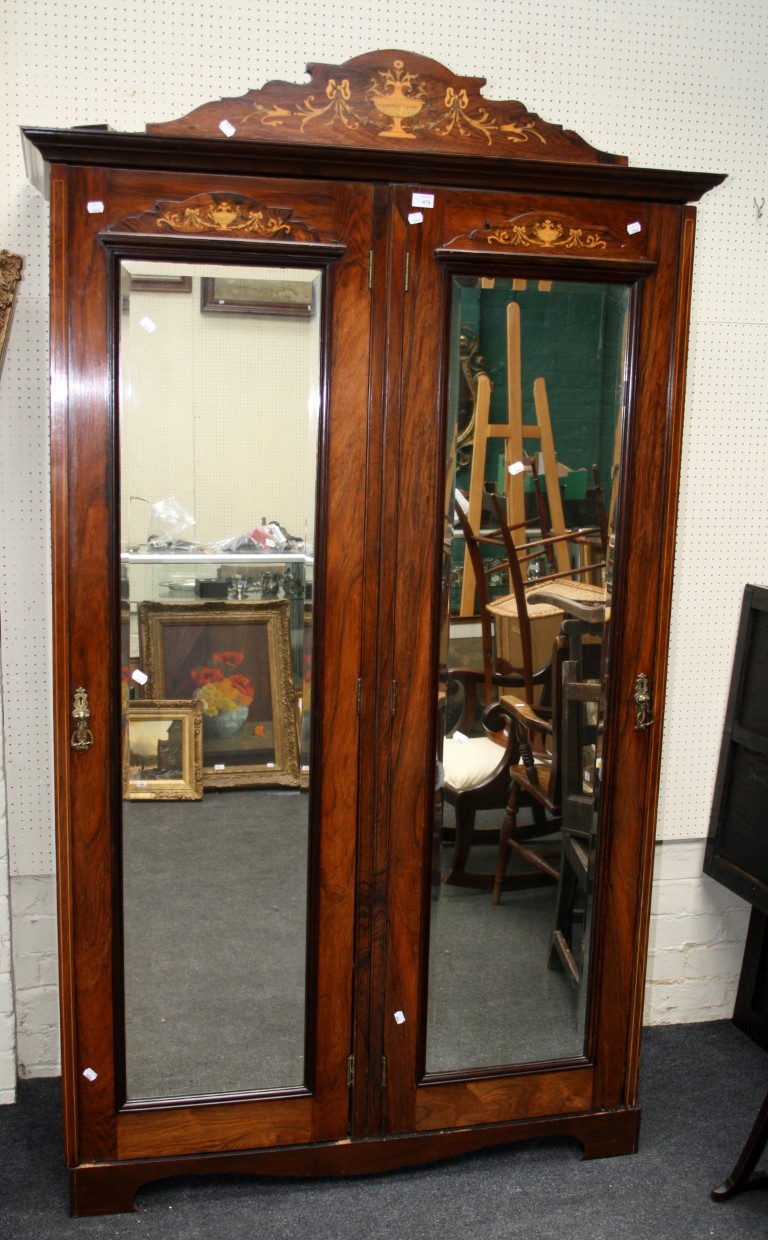 An Edwardian rosewood, marquetry inlaid and strung double wardrobe, the shaped pediment with urn and