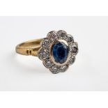 A sapphire and diamond cluster ring, the oval cut sapphire In a rub over-mount within a border of