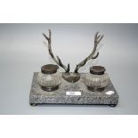 An early 20th century desk stand with EP stag trophy pen rest and twin facet cut lidded wells, on