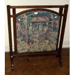 An Edwardian oak firescreen, the pierced frame enclosing a woolwork panel of Medieval figures on